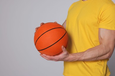 Athletic young man with basketball ball on light grey background, closeup