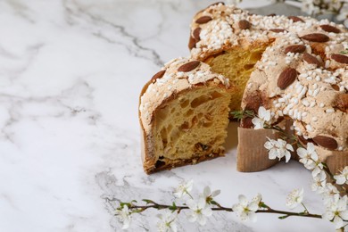 Photo of Delicious Italian Easter dove cake (traditional Colomba di Pasqua) and flowers on white marble table, closeup