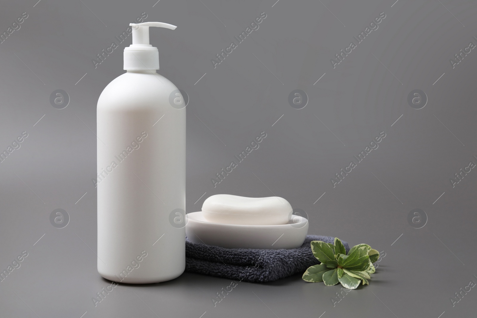 Photo of Soap bar, bottle dispenser and towel on grey background, space for text