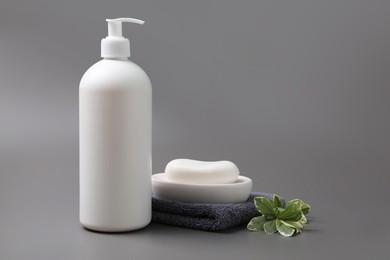 Photo of Soap bar, bottle dispenser and towel on grey background, space for text