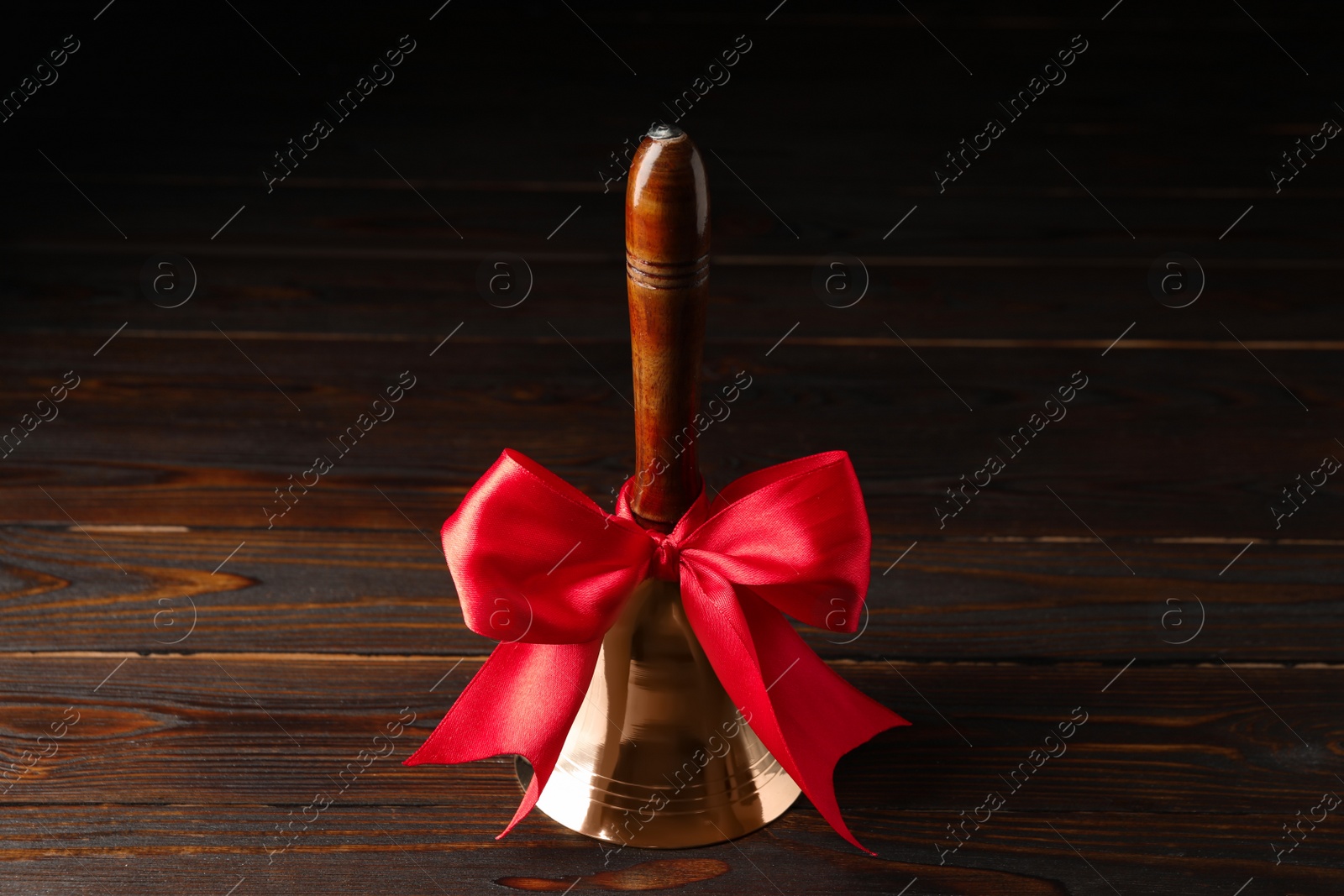 Photo of Golden bell with red bow on wooden table. School days