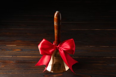 Golden bell with red bow on wooden table. School days