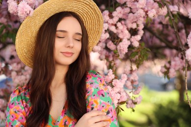 Photo of Beautiful woman in straw hat near blossoming tree on spring day, space for text