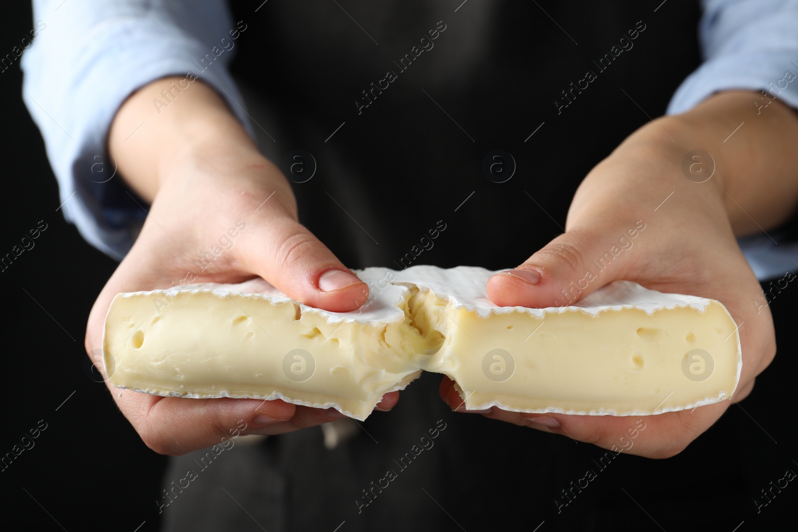 Photo of Woman breaking delicious brie cheese on black background, closeup