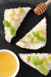 Delicious bruschettas with ricotta cheese, pear, mint and honey on dark table, flat lay