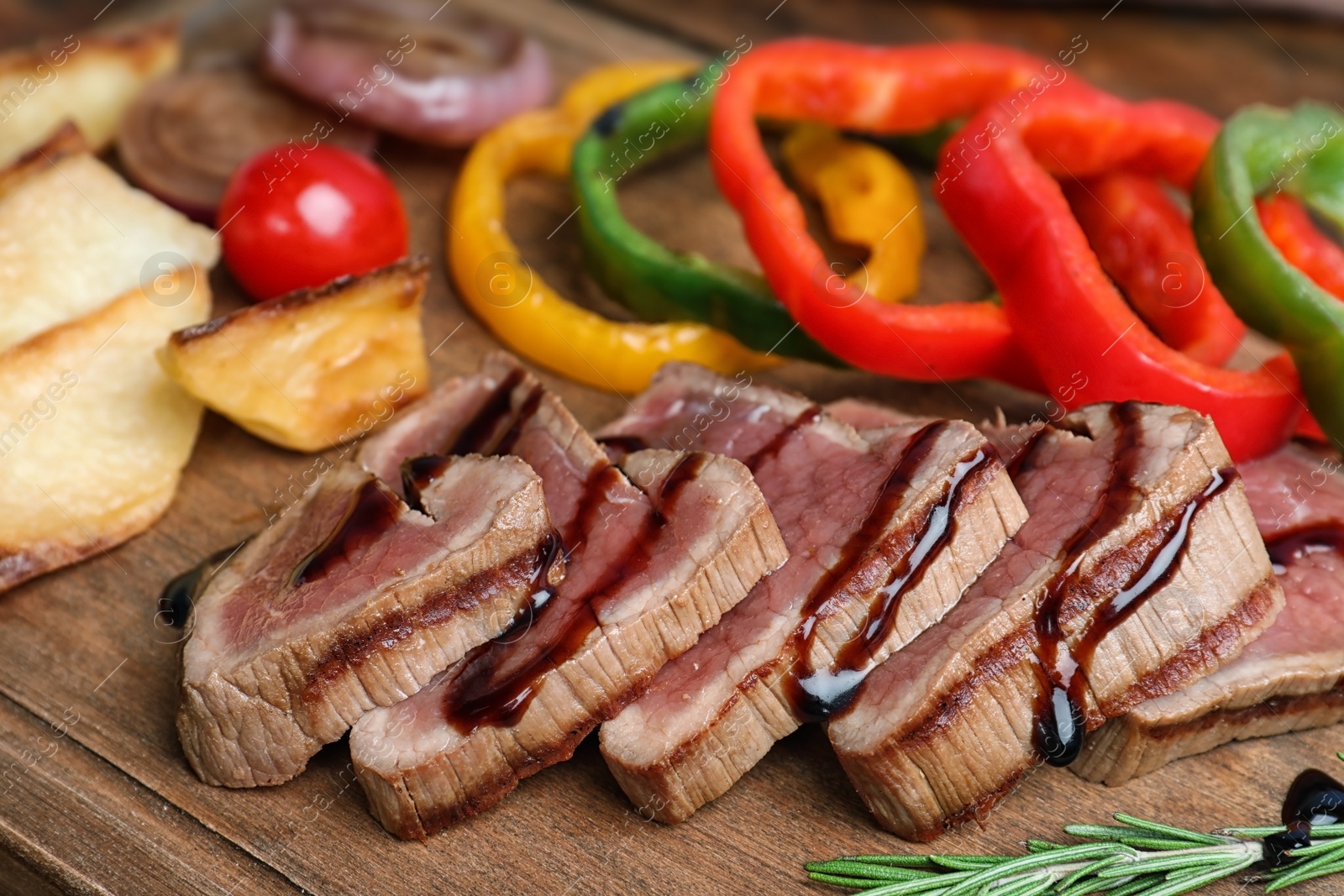 Photo of Cut roasted meat served with sauce and garnish on wooden board, closeup