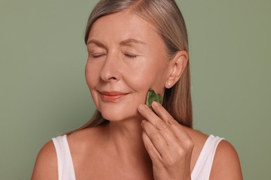 Photo of Woman massaging her face with jade gua sha tool on green background