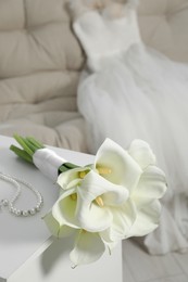 Photo of Beautiful calla lily flowers tied with ribbon and jewelry on white chest of drawers indoors