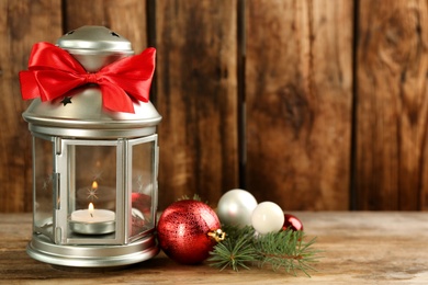 Photo of Christmas lantern with burning candle and festive decor on wooden table. Space for text