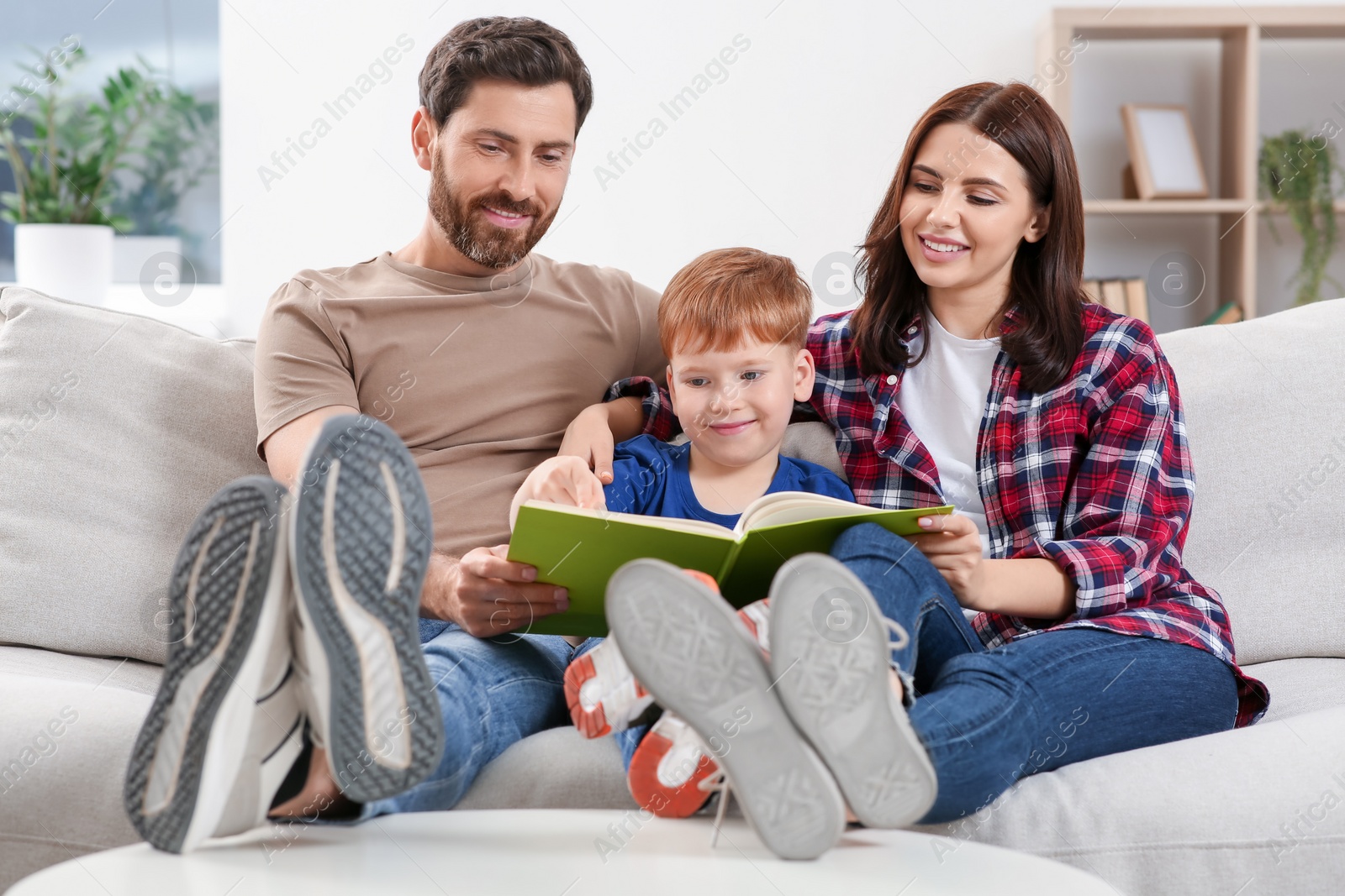 Photo of Happy parents with their child reading book on couch at home