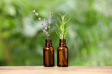 Photo of Bottles with essential oils, lavender and rosemary on wooden table against blurred green background