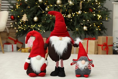 Photo of Funny Christmas gnomes on floor in room with festive decoration