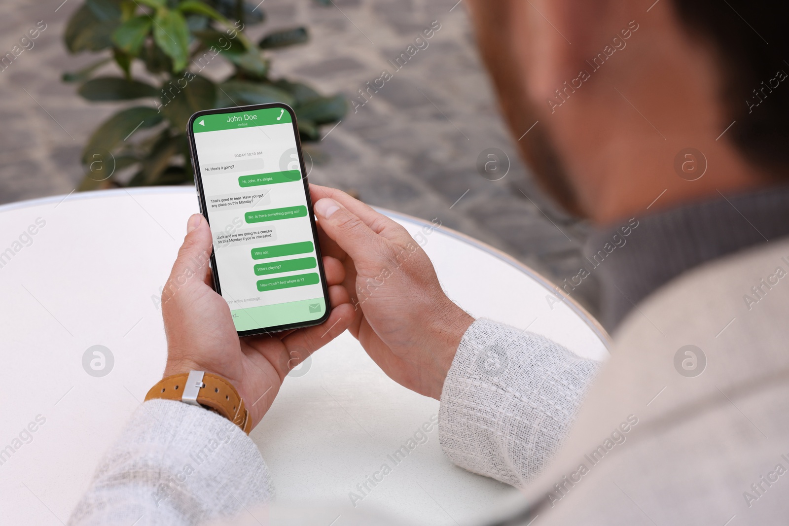 Image of Man texting via mobile phone at table outdoors, closeup. Device screen with messages