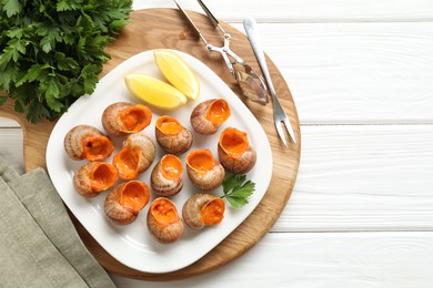 Photo of Delicious cooked snails served on white wooden table, flat lay. Space for text