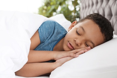 Cute little African-American boy sleeping in bed