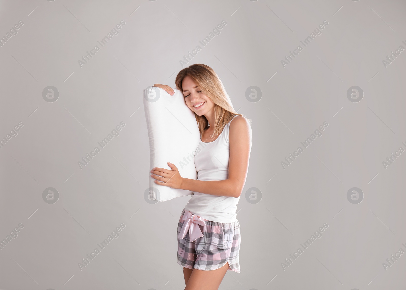 Photo of Young woman in pajamas embracing pillow on gray background