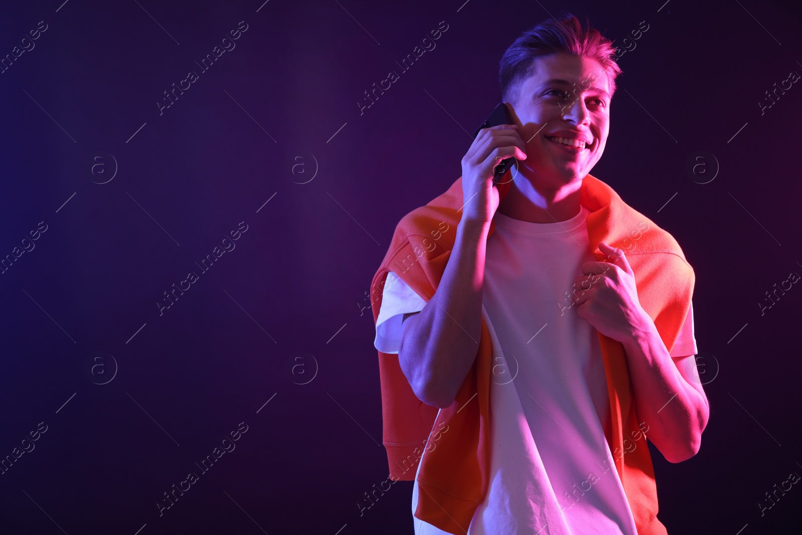 Photo of Young man talking on smartphone against dark background in neon lights. Space for text