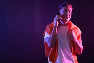 Young man talking on smartphone against dark background in neon lights. Space for text