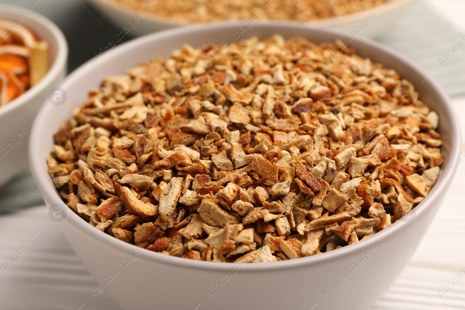 Photo of Bowl with dried orange seasoning zest on white wooden table, closeup