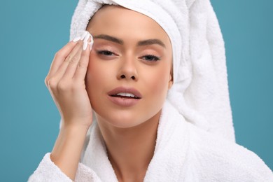 Beautiful woman removing makeup with cotton pad on light blue background