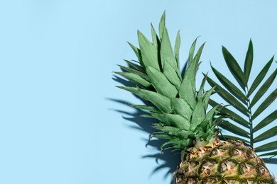 Photo of Whole ripe pineapple and green leaves on light blue background, flat lay. Space for text