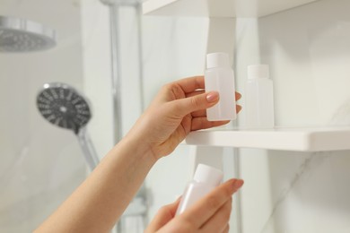 Chambermaid putting bottle of shampoo on shelf in hotel bathroom, closeup