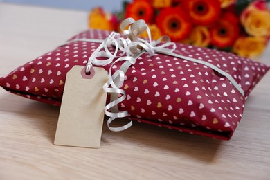 Photo of Parcel wrapped in heart patterned paper with cardboard tag on wooden table, closeup. Space for text