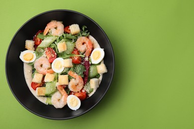 Photo of Delicious Caesar salad with shrimps on light green background, top view. Space for text