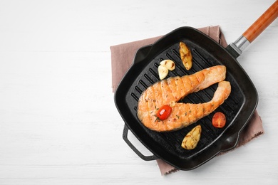 Frying pan with tasty salmon steak on wooden background