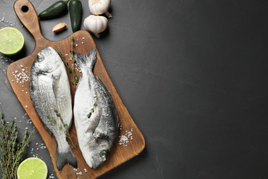 Flat lay composition with raw dorada fish on black table, space for text