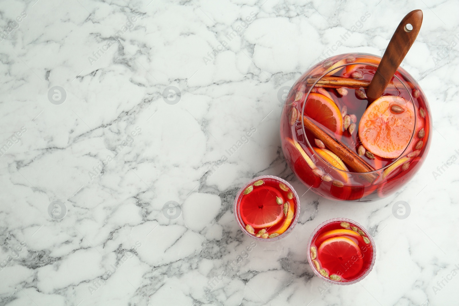 Photo of Glasses and bowl with aromatic punch drink on white marble table, flat lay. Space for text