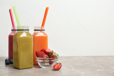 Photo of Bottles with healthy detox smoothies and bowl of strawberries on table