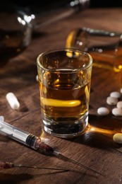 Photo of Alcohol and drug addiction. Whiskey in glass, syringes and pills on wooden table, closeup