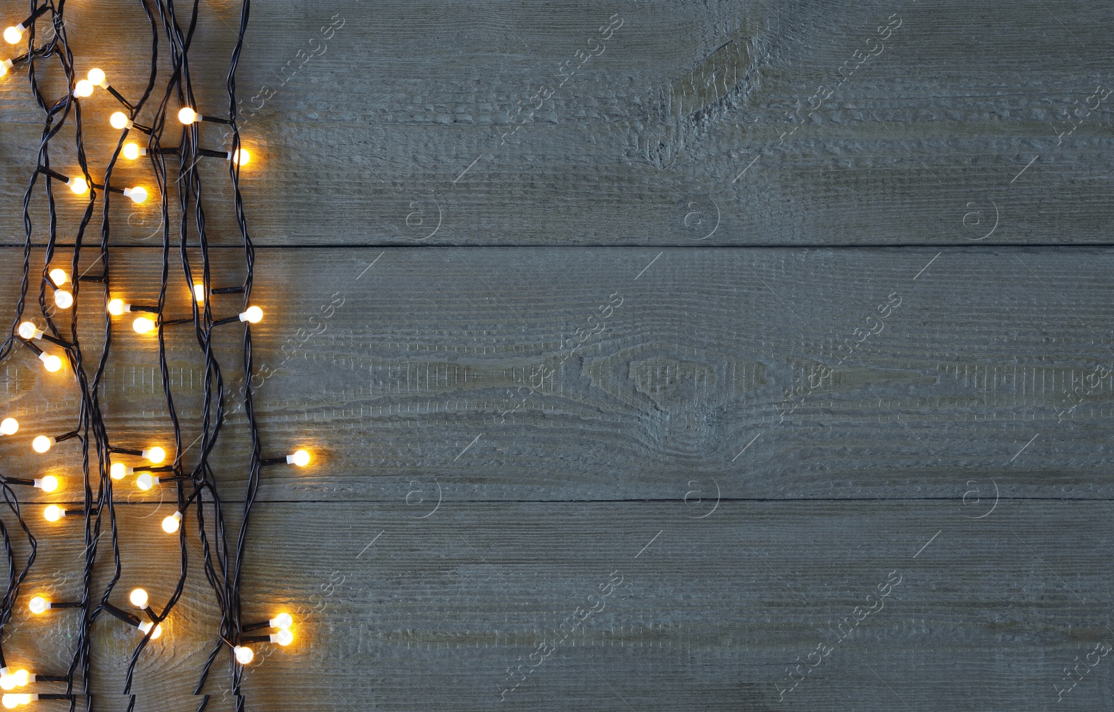 Photo of Christmas lights on wooden background, top view. Space for text