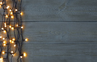 Photo of Christmas lights on wooden background, top view. Space for text