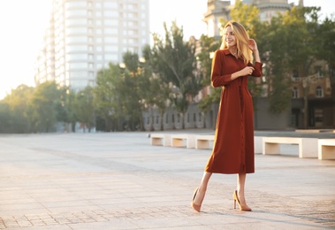 Beautiful young woman in stylish red dress on city street