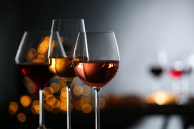 Glasses with different wines against defocused lights, closeup. Space for text