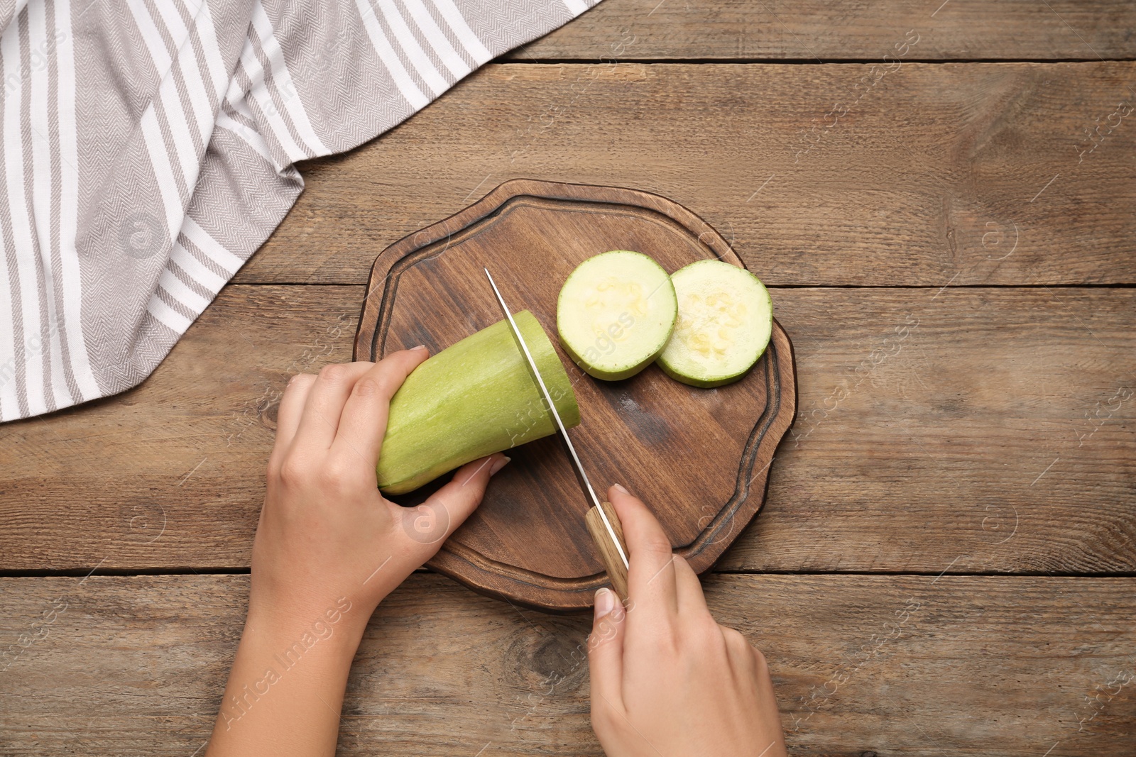 Photo of Woman cutting zucchini at wooden table, top view