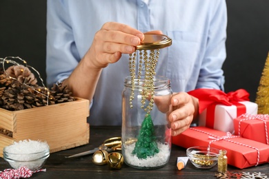 Woman making snow globe at black wooden table, closeup