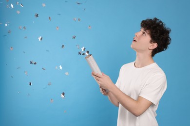 Photo of Happy teenage boy blowing up party popper on light blue background