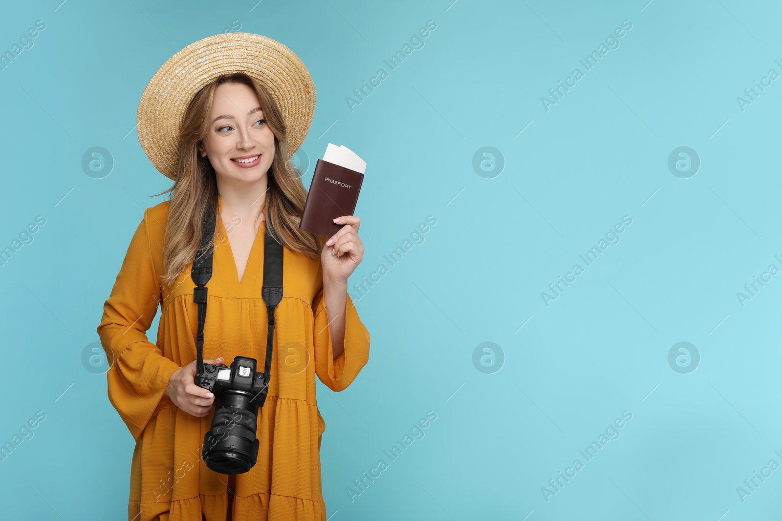 Photo of Happy young woman with camera, passport, ticket and hat on light blue background, space for text