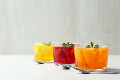 Photo of Glass bowls of natural jelly desserts on light table, space for text