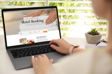 Image of Woman using laptop to book hotel at white wooden table, closeup