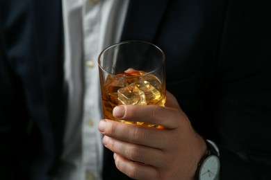 Photo of Man holding glass of whiskey with ice cubes on black background, closeup