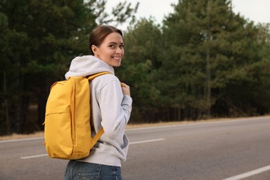 Happy young woman with backpack on road near forest