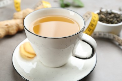 Photo of Cup of herbal diet tea, ginger and measuring tape on light table, closeup