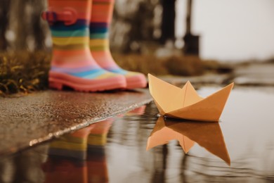 Photo of Little girl outdoors, focus on paper boat in puddle