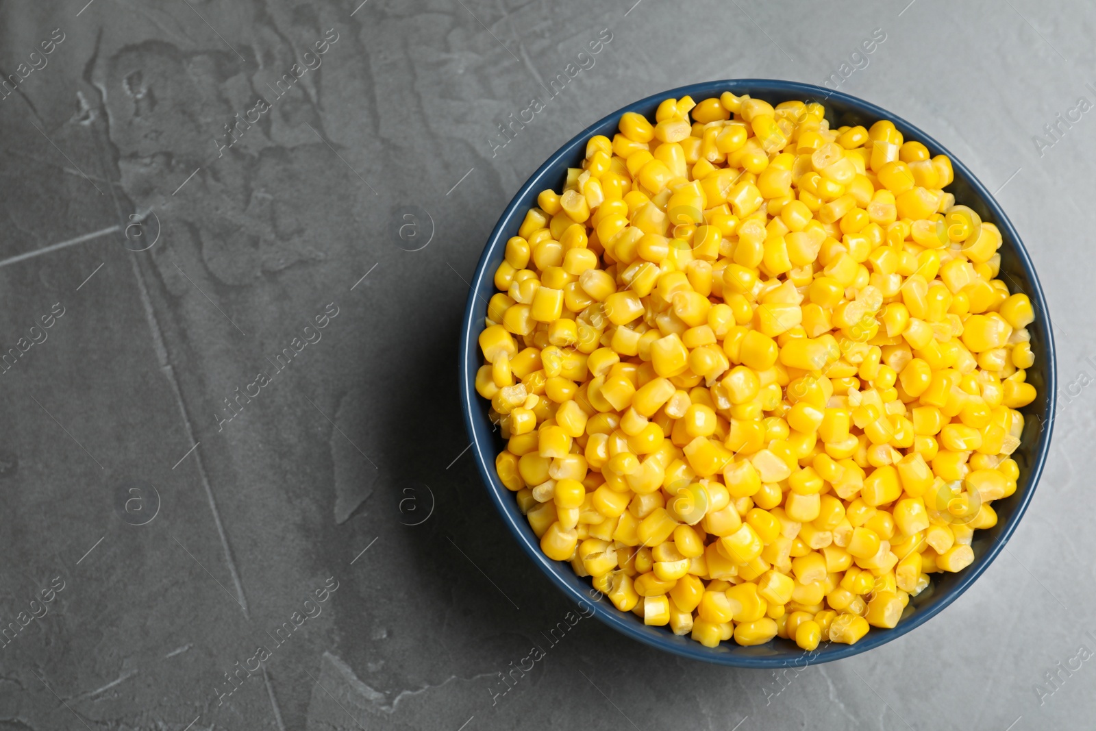 Photo of Delicious canned corn in bowl on grey table, top view. Space for text