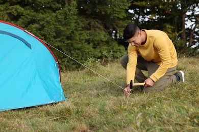 Man setting up blue camping tent near forest