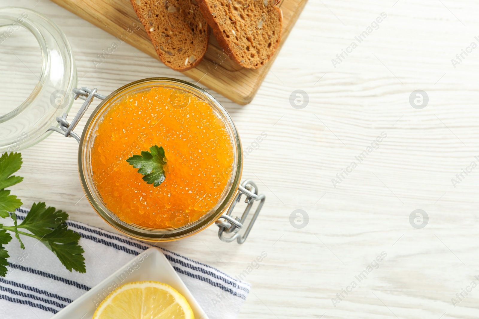 Photo of Fresh pike caviar in glass jar, bread and parsley on light wooden table, top view. Space for text